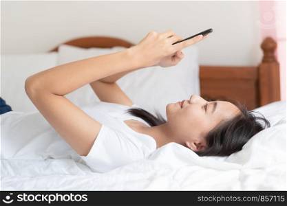 Beautiful young Asian women are using smartphone to chat with friend and Video call on the bed at her home