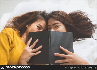 Beautiful young asian women LGBT lesbian happy couple kiss and smiling while lying together in bed under book at home. LGBT funny women after wake up. LGBT lesbian couple together indoors concept.