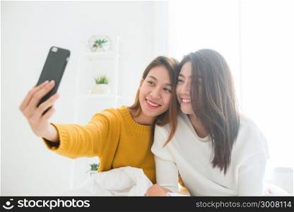 Beautiful young asian women LGBT lesbian happy couple sitting on bed hug and using phone taking selfie together bedroom at home. LGBT lesbian couple together indoors concept. Spending nice time home.