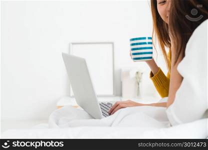 Beautiful young asian women LGBT lesbian happy couple sitting on bed hug and using laptop computer while drinking hot coffee cup together bedroom at home. LGBT lesbian couple together indoors concept.