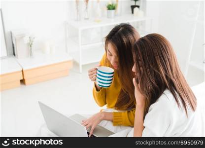 Beautiful young asian women LGBT lesbian happy couple sitting on bed hug and using laptop computer while drinking hot coffee cup together bedroom at home. LGBT lesbian couple together indoors concept.