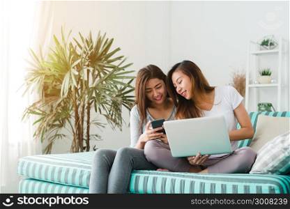 Beautiful young asian women LGBT lesbian happy couple sitting on sofa buying online using laptop a computer and phone in living room at home. LGBT lesbian couple together indoors concept.