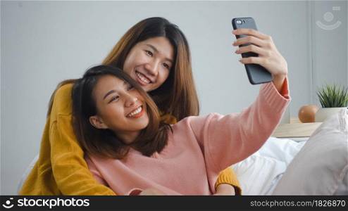 Beautiful young asian women LGBT lesbian happy couple sitting on sofa hug and using phone taking selfie together bedroom at home. LGBT lesbian couple together indoors concept. Spending nice time home.