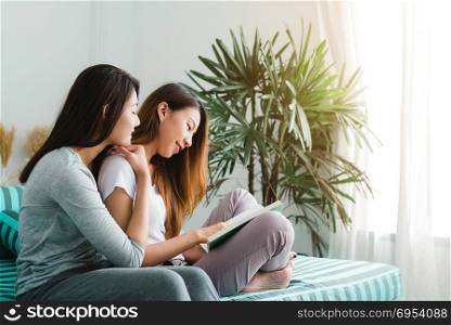 Beautiful young asian women LGBT lesbian happy couple sitting on sofa reading book together near window in living room at home. LGBT lesbian couple together indoors concept. Spending nice time at home