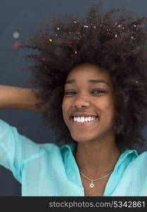 beautiful young black woman celebrating new year and chrismas party while blowing confetti decorations to camera isolated over gray background