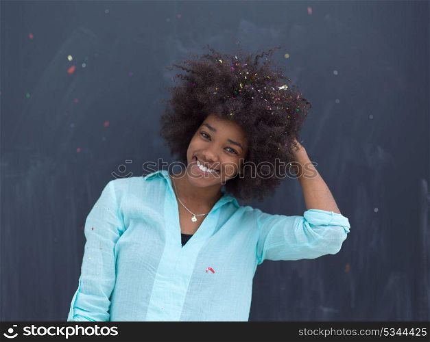 beautiful young black woman celebrating new year and chrismas party while blowing confetti decorations to camera isolated over gray background
