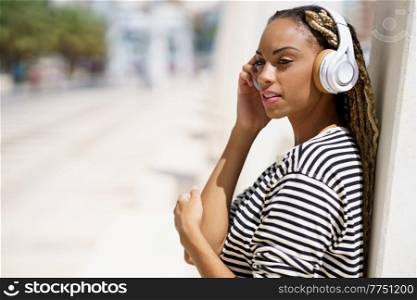Beautiful young black woman listening to music with wireless headphones outdoors.. Young black woman listening to music with wireless headphones outdoors.