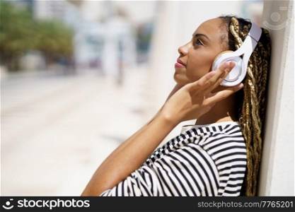Beautiful young black woman listening to music with wireless headphones outdoors.. Young black woman listening to music with wireless headphones outdoors.