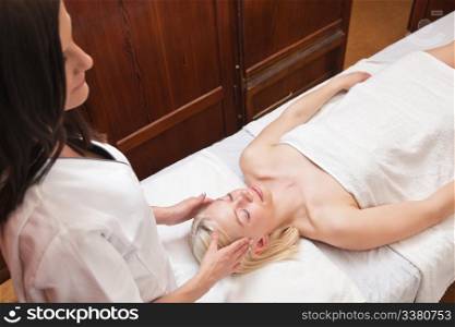 Beautiful young blond woman receiving head massage at spa