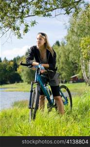 Beautiful young blond woman riding bicycle by lake summer day