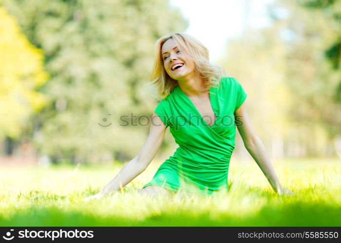 Beautiful young blond woman sitting on grass in park