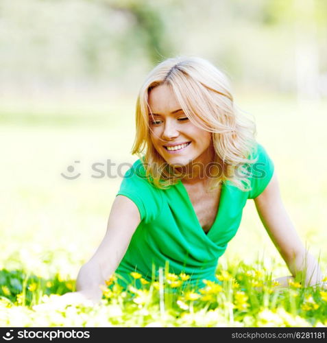 Beautiful young blond woman sitting on grass in park and enjoyng flowers