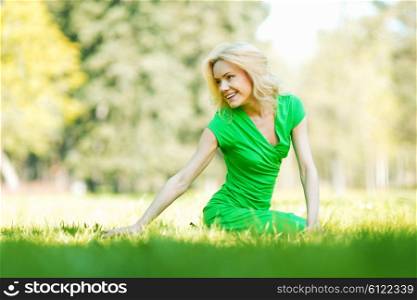 Beautiful young blond woman sitting on grass in park and enjoyng nature