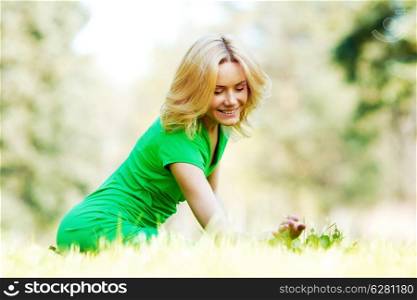Beautiful young blond woman sitting on grass in park and enjoyng nature