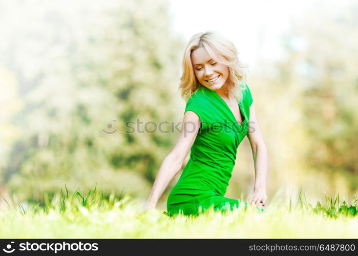 Beautiful young blond woman sitting on grass in park and enjoyng nature. Woman sitting on grass