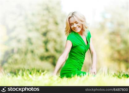 Beautiful young blond woman sitting on grass in park and enjoyng nature. Woman sitting on grass
