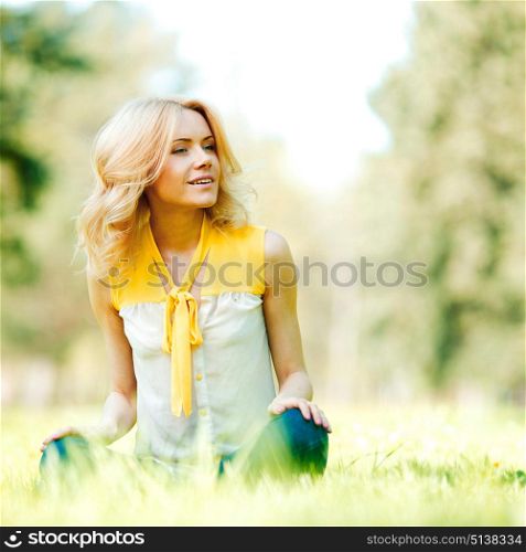 Beautiful young blond woman sitting on grass in park. Woman sitting on grass