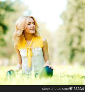 Beautiful young blond woman sitting on grass in park. Woman sitting on grass