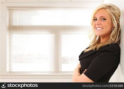 Beautiful young blond woman standing in front of window at office or school. Space for copy.
