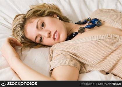 Beautiful young blonde in bed in a tan knit blouse