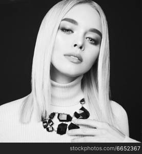 Beautiful young blonde with classic makeup and modern jewelry. Sexy lady pose in studio on gray background. Blue-eyed model in tightness turtleneck.