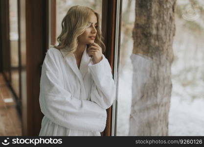 Beautiful young blonde woman in bathrobe relaxing at indoor swimming pool