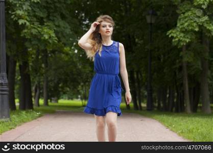 Beautiful young blonde woman in blue dress on the summer park