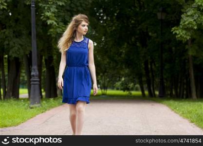 Beautiful young blonde woman in blue dress on the summer park