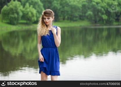 Beautiful young blonde woman in blue dress on the summer street