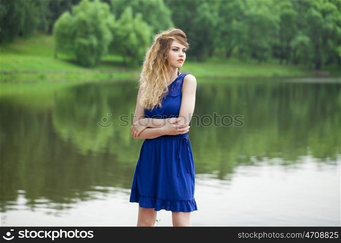 Beautiful young blonde woman in blue dress on the summer street