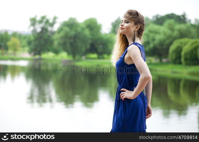 Beautiful young blonde woman in blue dress on the summer street