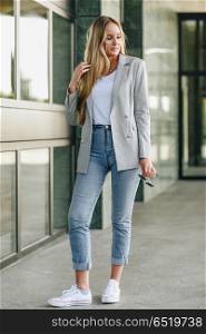 Beautiful young blonde woman in urban background.. Beautiful young caucasian woman in urban background. Blond girl wearing casual clothes in the street. Female with elegant jacket and blue jeans