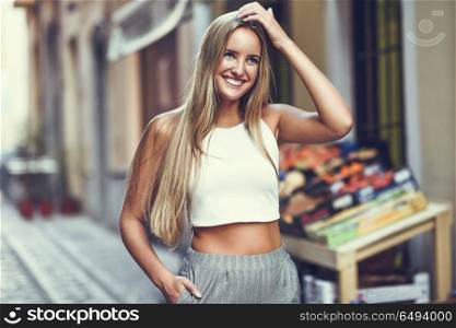 Beautiful young blonde woman smiling in urban background.. Smiling young woman in urban background. Blond girl wearing with nice hair casual clothes in the street. Straight hairstyle.