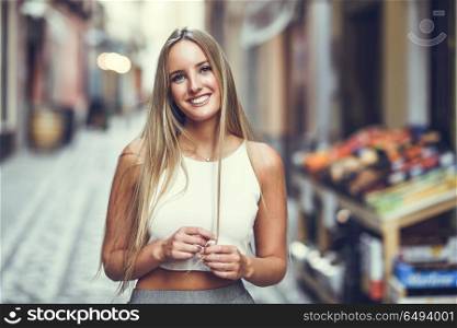 Beautiful young blonde woman smiling in urban background.. Smiling young woman in urban background. Blond girl wearing with nice hair casual clothes in the street. Straight hairstyle.