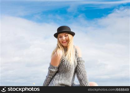 Beautiful young blonde woman wearing fedora hat and sweater jumper posing on sky background.. Woman wearing fedora and jumper outdoor