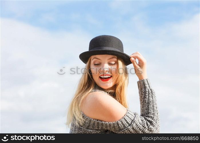 Beautiful young blonde woman wearing fedora hat and sweater jumper posing on sky background.. Woman wearing fedora and jumper outdoor
