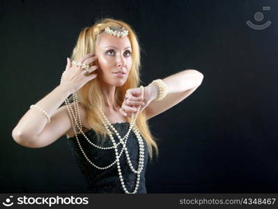 beautiful young blonde woman with long hair and a pearl beads on dark background.