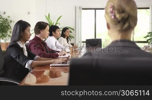 Beautiful young blonde woman working as manager and smiling at camera during business meeting with colleagues. Rack focus
