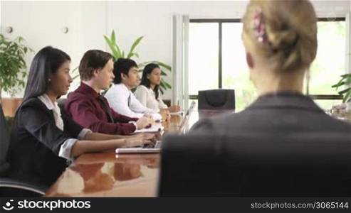 Beautiful young blonde woman working as manager and smiling at camera during business meeting with colleagues. Rack focus