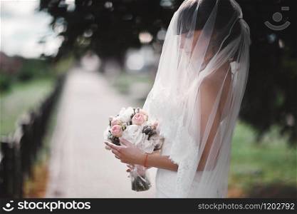 Beautiful young bride in a white luxury dress and in a bridal veil with a bouquet of flowers posing outdoor. wedding portrait. copy space.. Beautiful young bride in a white luxury dress and in a bridal veil with a bouquet of flowers posing outdoor. wedding portrait. copy space