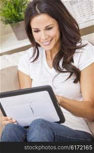 Beautiful young brunette woman at home sitting on sofa or settee using her tablet computer or iPad and smiling