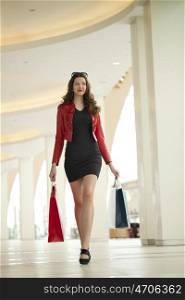 Beautiful young brunette woman in a black dress, holding shopping bags walking in the shop