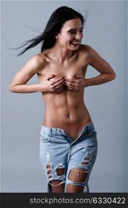 Beautiful young brunette woman wearing broken blue jeans. Beautiful topless girl with moving straight hair laughing. Studio shot.