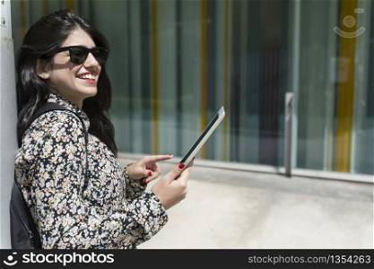 Beautiful young businesswoman holding tablet in her hands against urban city background.