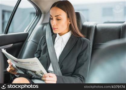 beautiful young businesswoman traveling by car reading newspaper