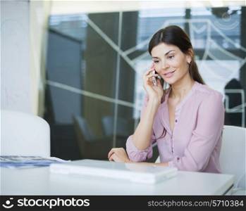 Beautiful young businesswoman using mobile phone at conference table