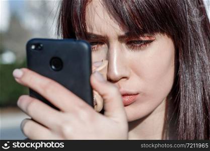 beautiful young Caucasian brown haired girl puts Foundation on her face using the phone as a mirror