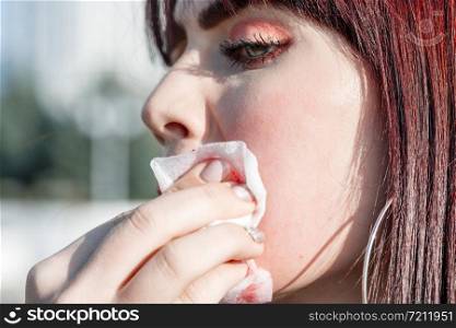 beautiful young Caucasian brown haired girl removes smeared lipstick from her face in the street