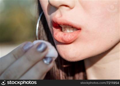 beautiful young Caucasian brown haired girl removes smeared lipstick from her face in the street
