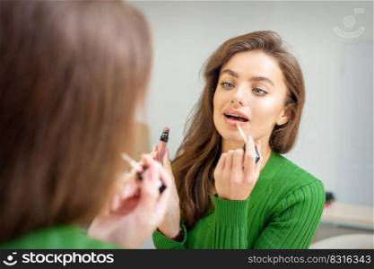 Beautiful young caucasian woman applying gloss to the lips looking in the mirror. Woman applying gloss to the lips
